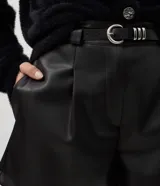 Short de poliuretano color negro, de corte recto con pinzas frontales y largo corto. Incluye un cinturón fino con hebilla y pasantes metálicos.