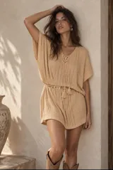Poncho corto de tejido de punto en color beige, con mangas cortas amplias, escote en V con cordones entrelazados y terminaciones con borlas.