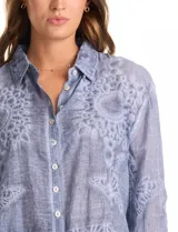 Camisa de algodón color gris con bordados florales en el frente y las mangas. Tiene cuello con solapa y cierre frontal con botones.