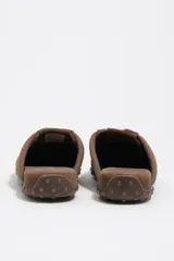 Zapatilla estilo mula de color beige, confeccionada en una combinación de algodón y serraje vacuno, con suela de caucho con tachuelas texturizadas y costuras decorativas visibles en la parte superior.