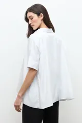 Camisa blanca de corte oversized, confeccionada en algodón, con cuello clásico, cierre frontal de botones y mangas cortas con vuelta.