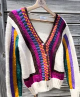 Cardigan tejido a mano en lana merino, con diseño multicolor de bloques geométricos y rayas en tonos blanco, marrón, rosado, celeste y verde. Presenta escote en V, mangas largas y cierre frontal con botones.