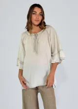 Blusa verde oliva de corte holgado, con cuello redondo con volantes y abertura en V con lazo. Tiene mangas 3/4 acampanadas y ruedo asimétrico.