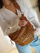 Riñonera de gran tamaño confeccionada en cuero con frente de pelo vacuno estampado con diseño animal print de leopardo. Cuenta con correa ajustable de cuero en color suela, cierre metálico y parche de marca grabado en el frente.