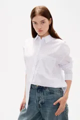 Camisa de algodón blanca con estampado de corazones formados por pequeños cristales de strass. Presenta cuello clásico, cierre frontal con botones, bolsillo en el pecho y mangas largas con puños abotonados.
