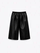 Bermuda de pierna amplia y largo cropped, confeccionada en cuerina negra con acabado levemente brillante. Presenta pretina elástica, pinzas frontales que aportan volumen, bolsillos laterales y un bolsillo ojal en la parte trasera.