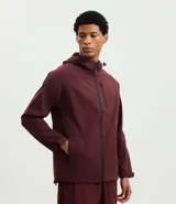 Campera deportiva Get Over de tejido técnico resistente al agua, color bordó. Presenta capucha ajustable con cordones, cierre frontal con cremallera, bolsillos laterales y un bolsillo adicional en el pecho, todos con cierre.