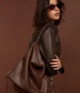 Bolso hobo grande desestructurado color marrón oscuro, con correa de mano y correa larga desmontable. Presenta cierres laterales ajustables con tiradores y cierre superior.