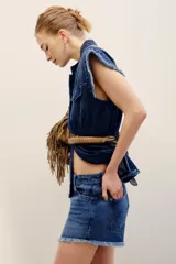 Short de denim azul medio con diseño de cinco bolsillos, cierre frontal con botones y bordes desmechados en el ruedo.