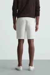 Bermuda negra de corte recto, con cintura elástica ajustable mediante cordón, pliegues frontales y bolsillos de vivo en la espalda. El bajo tiene un dobladillo vuelto.