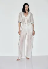 Mono largo de mujer confeccionado en organza transparente, con escote en V con cierre frontal, mangas cortas con puños acanalados a rayas y cintura ajustable con cordón. Presenta un diseño de pierna ancha con bolsillos tipo cargo en los laterales.