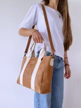 Bolso tipo tote de cuero color camel con dos tiras verticales blancas y correa larga ajustable al hombro.