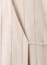 Vestido midi cruzado beige con sutiles rayas verticales oscuras, cuello camisero con solapa, mangas largas y cierre delantero cruzado.