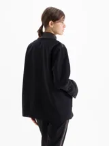 Chaqueta negra de corte recto con largo hasta la segunda cadera. Presenta detalles de cuero en cuello, frente, hombros y puños, con cuello decorado con tachas metálicas y punteras. Cuenta con bolsillos frontales tipo cargo.