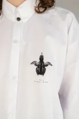 Camisa blanca de algodón con cuello con lengüeta y botón labrado, manga larga con puños y botones, corte oversize y estampado de aves en el delantero.