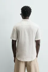 Camisa de lino color beige de corte relajado, con cuello solapa, manga corta y cierre frontal con botones.