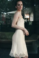 Vestido midi de estilo lencero confeccionado en tejido satinado color beige. Presenta escote recto con tirantes finos y aplicaciones de encaje a tono en el escote y en el ruedo.