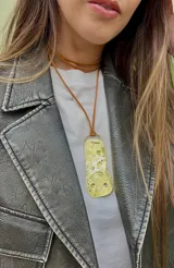 Collar con dije irregular de bronce con textura irregular y detalles grabados, colgando de un cordón de cuero sintético marrón. Incluye un choker de cuero sintético marrón.