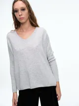 Sweater de tejido de punto suave con escote en V, manga larga y corte holgado. Presenta aberturas laterales en el ruedo y un detalle distintivo en la espalda.