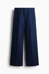 Pantalón de jean tipo wide leg de tiro alto, confeccionado en denim rígido de color azul oscuro. Presenta un corte holgado desde el muslo hasta el ruedo, con raya marcada en el centro de las piernas, cierre con botón oculto y bolsillos al bies.