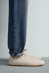 Zapatilla de cordones para hombre, confeccionada en piel con acabado de serraje en color beige. Presenta un diseño de perfil bajo con detalles de pespuntes decorativos y una suela ultrafina.