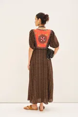 Vestido largo de viscosa con estampado geométrico en tonos marrones y detalle de bordado colorido en el escote en V. Presenta mangas cortas con frunces y puños elásticos, cintura elástica y cierre lateral invisible.