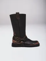 Bota de caña alta estilo western confeccionada en cuero con acabado avejentado. Presenta punta cuadrada, taco bajo y una correa con estribo metálico desmontable que rodea el tobillo.
