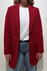Tapado de paño de lana color rojo, con diseño clásico de solapas, cierre frontal de dos botones y bolsillos con solapa. Presenta un corte estructurado con tajo en la parte posterior y forro interior.