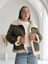 Chaqueta verde militar de gamuza sintética con interior de piel sintética color crema. Tiene cierre frontal con cremallera, cuello con solapas grandes y cinturón con hebilla en los puños.