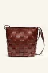 Cartera tipo morral de cuero color beige, con diseño trenzado artesanal, correa larga regulable y cierre superior.