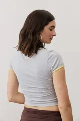 Remera corta gris melange con ribetes amarillos en el cuello y las mangas, y un estampado gráfico abstracto en el pecho.