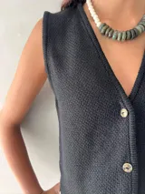 Chaleco negro de punto con cuello en V y cierre frontal con botones.