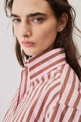Camisa a rayas verticales en tonos rosado y marrón, de manga larga abullonada, cuello camisero y cierre frontal de botones con pequeños apliques brillantes.