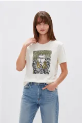 Remera color off-white de manga corta y cuello redondo, con estampa frontal artística de rostro con detalles en verde, negro y dorado.