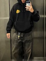 Canguro negro de corte oversize con capucha y bolsillo frontal. Presenta un diseño gráfico estampado en la espalda que simula un paquete de yerba mate, con la ilustración de una mujer, hojas y la inscripción 'La Volada'.