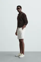 Bermuda negra de corte recto, con cintura elástica ajustable mediante cordón, pliegues frontales y bolsillos de vivo en la espalda. El bajo tiene un dobladillo vuelto.