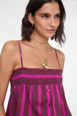 Top de algodón con diseño de rayas verticales en tonos bordó y fucsia. Presenta tirantes finos regulables, escote recto con fruncido elástico en el pecho, botones frontales decorativos y corte acampanado.