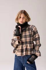 Blusa de manga larga con estampado a cuadros en tonos beige y negro, cuello alto con volados, diseño fruncido en el pecho y las mangas, y terminación acampanada en los puños y el bajo.