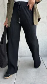 Pantalón de tejido de punto acanalado en color negro, con corte recto y ligeramente acampanado en el bajo. Presenta una cintura elástica con cordón ajustable y terminaciones con herrajes metálicos.