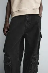 Pantalón cargo de denim lavado negro, corte relajado y tiro medio. Presenta múltiples bolsillos cargo con solapa y detalle de cierre en las perneras, además de bolsillos de vivo traseros. El bajo es ajustable con trabilla.