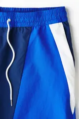 Short de baño y deportivo confeccionado en nylon, de corte holgado. Presenta un diseño de bloques de color en tonos azul, azul marino y blanco. Cuenta con cintura elástica con cordón ajustable blanco, bolsillos laterales y aberturas en los costados del ruedo. Incluye suspensor interno de malla.