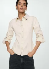 Camisa de estilo vaquero confeccionada en algodón, con cuello camisero, cierre frontal con botones metálicos y mangas largas con puños abotonados. Presenta un diseño entallado con costuras frontales.