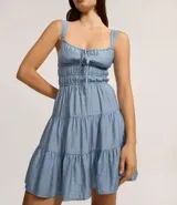 Vestido corto de silueta evasé color celeste, con escote recto y detalle de lazo en el centro. Posee breteles medianos, cintura elástica fruncida y falda con volados escalonados.