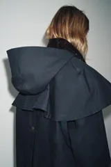 Trench azul marino con cuello de pana marrón y capucha desmontable con interior a cuadros. Tiene charreteras, canesú, bolsillos con solapa y cierre frontal con cremallera y botones a presión ocultos.