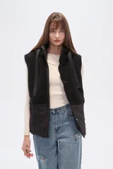 Chaleco con capucha, diseño bicolor que combina textura de corderito en la parte superior y material técnico liso en la parte inferior. Cuenta con cierre frontal y botones a presión.