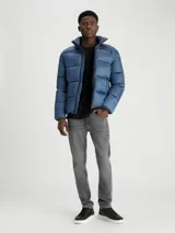 Campera acolchada azul con cuello alto, cierre frontal con cremallera, bolsillos laterales con cremallera, puños y dobladillo con punto canalé y logo de Calvin Klein bordado en el pecho.