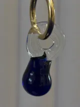 Aros tipo argolla dorada con dije colgante de vidrio soplado en forma de lágrima, combinando una parte transparente con una base en color azul intenso.