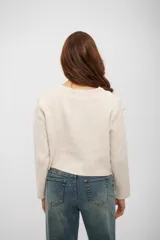 Saco de punto color beige, con cuello redondo, cierre frontal de botones oscuros y dos bolsillos delanteros. De corte recto y manga larga.