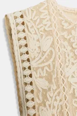 Vestido midi de viscosa con efecto arrugado, cuello redondo y diseño sin mangas. Presenta una sobrecapa superior con bordados detallados y entredoses, con cordones laterales ajustables terminados en borlas.