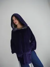 Buzo tipo canguro oversize de tela plush, color azul claro. Presenta capucha, cierre frontal parcial con cordón turquesa y bolsillos canguro frontales. Las mangas son largas y abullonadas con puños ajustados.